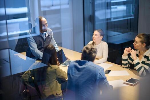 Diverse business team gathered around a table discussing analytics during a meeting in a modern office. Laptop screen shows charts and graphs, symbolizing teamwork, communication, and data driven photo