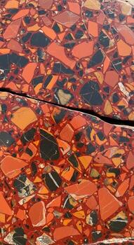 Abstract mosaic pattern of fractured red orange and black stone fragments creating a vibrant and textured surface with a central crack photo