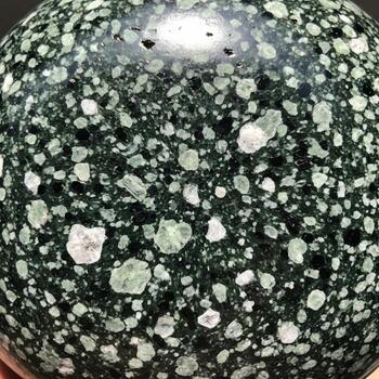 Close up view of a dark green speckled sphere with lighter green and white inclusions creating a unique natural pattern photo