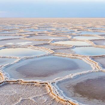 Vast expanse of a surreal salt flat with hexagonal patterns of shallow water and mineral deposits under a clear sky photo