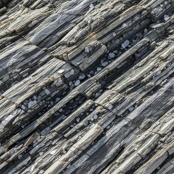 Close up abstract view of weathered layered rock formations with diagonal striations and varied textures in natural light photo