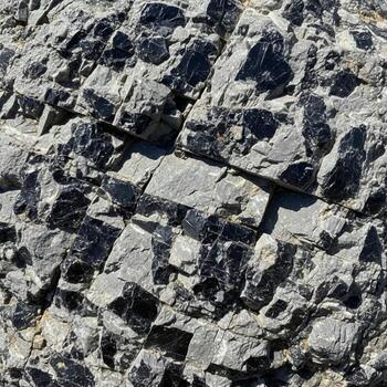 Close up view of rough textured gray rock with sharp angular fragments and a dark shadow creating contrast photo
