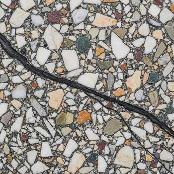 Close up view of a cracked terrazzo floor with a mosaic of colorful aggregate pieces and a dark line running through it photo