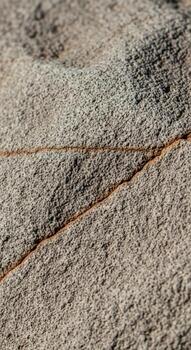 Close up view of a textured weathered rock surface with a distinct reddish brown crack running diagonally across the frame photo