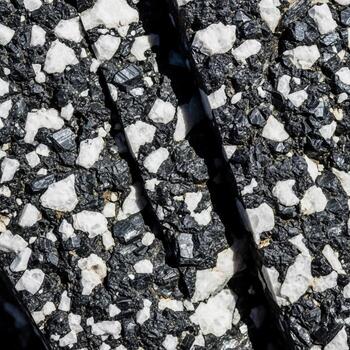 Close up abstract texture of asphalt pavement with white aggregate chips and a dark crack running through the surface photo