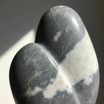 Smooth polished stone sculpture with marbled grey and white patterns abstract organic form casting a soft shadow photo