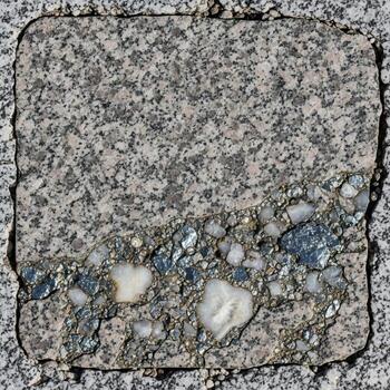 Close up view of a weathered textured concrete paver with embedded pebbles and a small patch of moss creating a natural abstract pattern photo