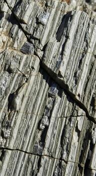 Close up view of a weathered rock surface showcasing intricate striations and dark mineral inclusions creating a natural abstract pattern photo