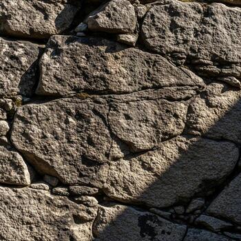Rough hewn stone wall texture with sunlight and shadow patterns creating depth and visual interest photo