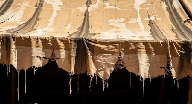 A close up view of a weathered and tattered fabric canopy with decorative scalloped edges and hanging threads photo