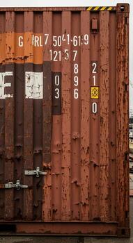 Close up view of a weathered rusty orange shipping container with identifying marks and numbers visible on its corrugated metal side photo