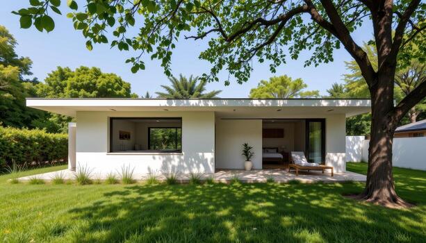 A low minimalist home with open windows surrounded by natural grass and tree shade. photo