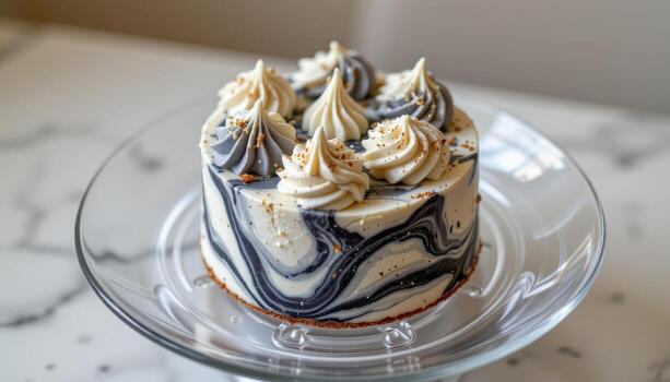 A marble patterned mini cake with gray and white swirls on a transparent glass plate. photo