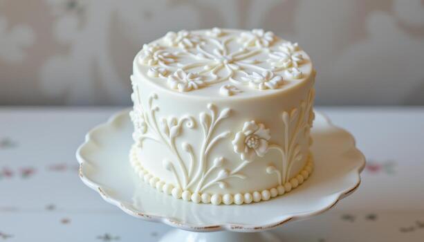 A white fondant mini cake with elegant embossed floral patterns on a porcelain cake stand. photo