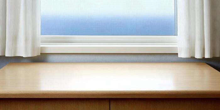 An empty light wood table with a shiny surface sits in front of a white framed window with translucent glass and white curtains photo