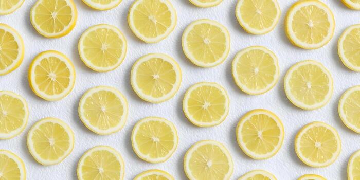 Fresh yellow lemon slices are arranged in a pattern on a textured white background creating a bright and clean image photo