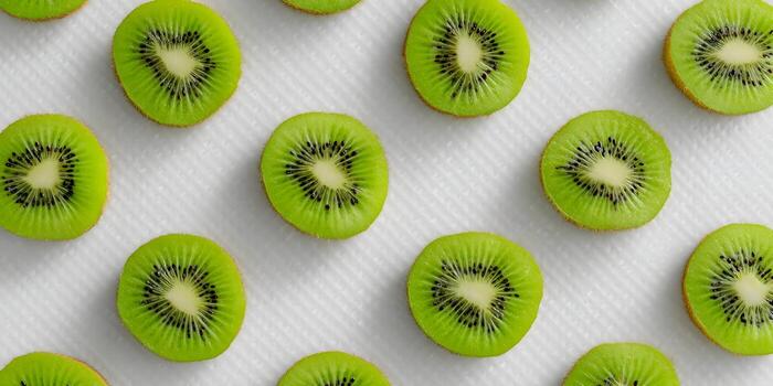 Many fresh kiwi fruit slices are arranged in an appealing pattern on a textured white background photo