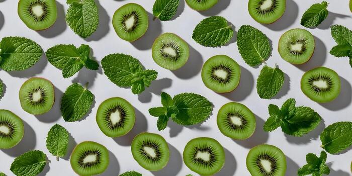 Fresh green kiwi slices and mint leaves are arranged in a repeating pattern on a light background photo