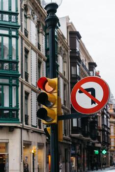 Traffic signal displaying red light and yellow caution light alongside no left turn sign on urban street with historic buildings in the background, emphasizing road safety and navigation photo