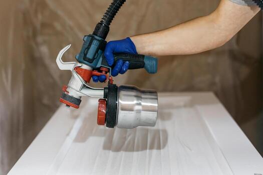 Skilled individual using a paint sprayer with a metallic container, applying paint to a smooth surface, showcasing the precision of the painting process in a workshop environment photo
