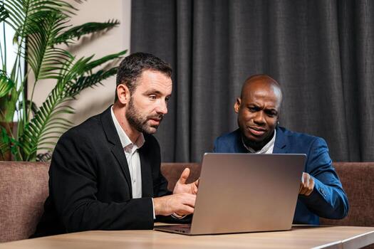 Two business professionals engaged in a discussion while analyzing data on a laptop, surrounded by indoor plants, showcasing collaboration and problem-solving in a modern workspace photo