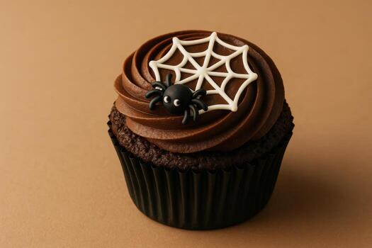 Mix of Halloween food horror and humor. Close-up of single chocolate cupcake with small sugar spider and web icing, in matte black wrapper. Isolated warm beige background photo
