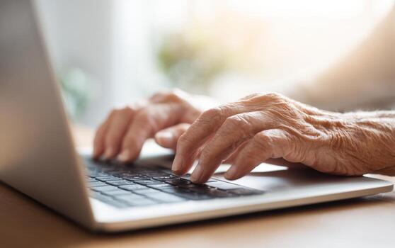 Elderly hands skillfully typing on a laptop keyboard in a bright and inviting workspace during daytime photo