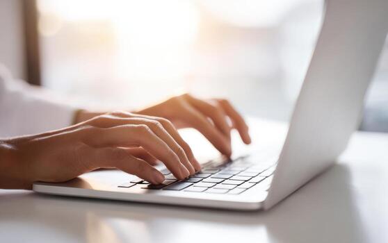 Hands type swiftly on a laptop keyboard in a bright office setting, possibly at daytime photo