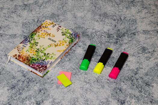 Colorful stationery items including a floral notebook, sticky notes, and vibrant highlighters arranged on a textured surface, creating an inviting workspace atmosphere for creativity and organization photo