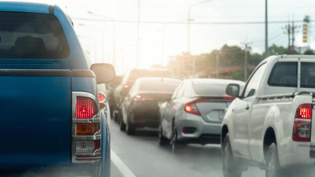 Rear side of pickup car blue color with turn on brake light. Environment of cars queue up in traffic jams. Pollution or fog after rain. Background of green tree and city. Queue up in traffic jams. photo