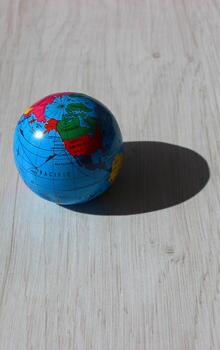 A vertical photo of a globe with the American continents visible in the light and its shadow cast on a wooden plank