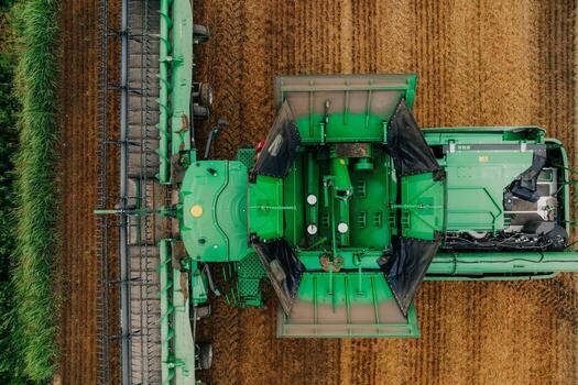 Aerial view of a green combine harvester working in a field with visible rows of harvested and unharvested crops, contrasting green and golden tones. photo