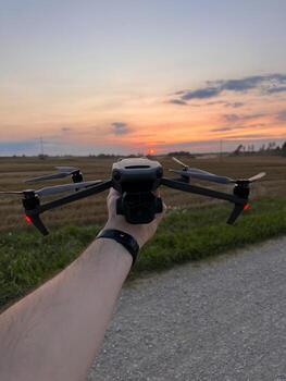 Drone with Red Indicator Lights Held Against a Sunset in Open Field photo