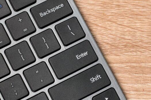 Close up view of a computer keyboard on wooden table with focus on Enter Key photo