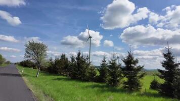 panoramico paesaggio transizioni a partire dal un' solitario albero per un' vento turbina, in mostra lussureggiante verdura e vivace nuvole, con un' liscio telecamera padella cattura il sereno ambiente video