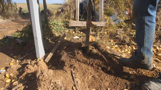 post secured properly, fence post fixed securely in ground, worker stabilizes fence post through backfill and tamping, fence post stabilization includes backfilling and soil compaction photo