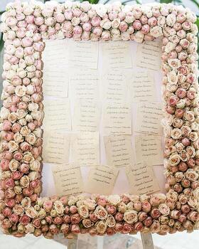 Event seating chart with guest names and table numbers, bordered by a frame of pink roses for special occasion. photo
