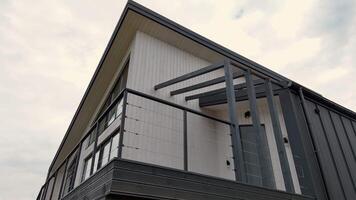modern en ram stuga Fasad med en eleganta balkong och minimalistisk svart räcke, låg vinkel skott av samtida triangel- arkitektur mot en molnig himmel video
