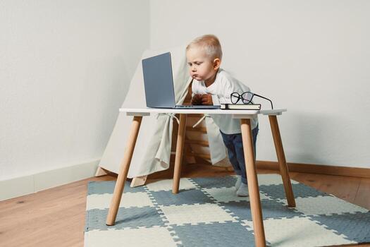 In a cozy workspace, a curious toddler explores a laptop, highlighting the importance of playful learning and early tech exposure for child development during critical formative years photo