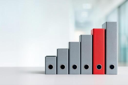 File Binders Arranged Like a Bar Graph on a Desk in an Office Setting, Highlighting a Single Red Binder Among Gray Ones to Showcase Organization and Growth photo