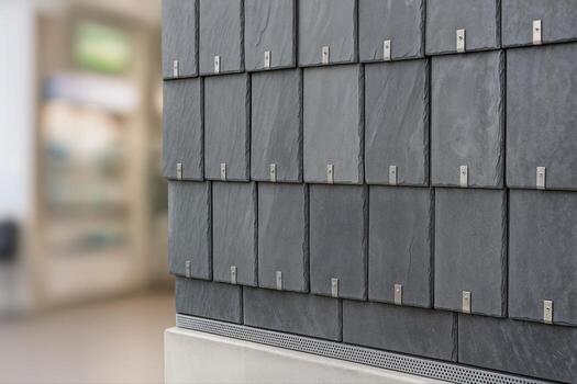 Slate Wall Design Featuring Uniformly Arranged Dark Tiles Mounted Vertically with Metal Fixtures Indoors, Emphasizing Modern Architectural Decor With Shallow Depth Of Field photo
