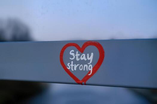 Graffiti Heart with 'Stay Strong' Message on Metal Railing Outdoors During Sunset With Shallow Depth of Field and Blurred Background photo
