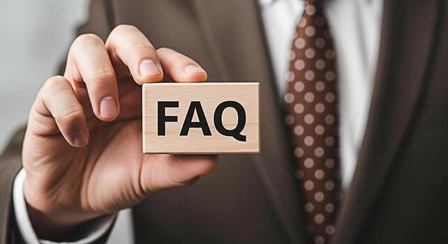 Professional businessman in a suit holding a wooden block with the text FAQ frequently asked questions in a corporate setting representing support guidance and information access photo