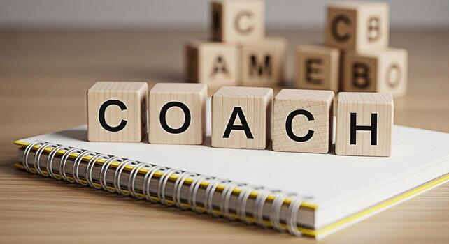 Wooden blocks spelling COACH resting on a spiral notebook on a wooden desk symbolizing guidance mentorship and support in a learning and development environment fostering a positive and motivational a photo
