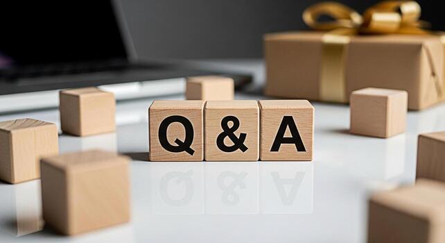 Wooden blocks displaying Q A on a reflective white surface with a laptop and gift box in the background representing knowledge sharing and customer support in a modern business setting photo