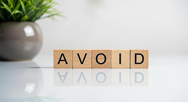 Wooden blocks spelling AVOID on a reflective white surface with a green plant in the background representing prevention caution and the importance of making informed decisions in a clean minimalist se photo