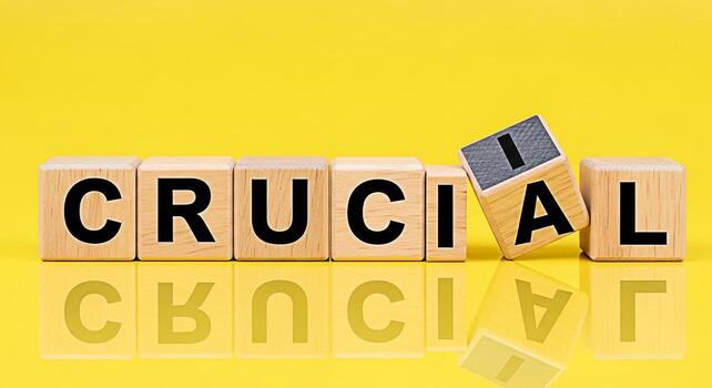 Wooden blocks spelling CRUCIAL on a yellow reflective surface emphasizing the importance of a key element creating a sense of urgency and focus on what truly matters for success and achievement photo