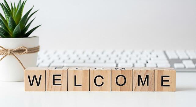 Wooden blocks spelling Welcome on a white desk next to a potted succulent plant and a computer keyboard creating a warm and inviting atmosphere for new beginnings and positive vibes photo