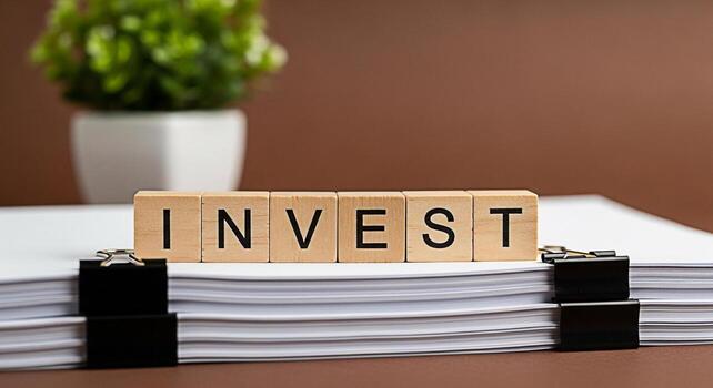Wooden blocks spelling INVEST resting on a stack of papers in a professional setting symbolizing financial planning growth and the importance of strategic investment for a secure future photo