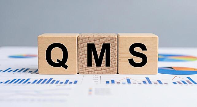 Wooden blocks displaying QMS acronym sitting atop financial charts in a bright office environment representing quality management system implementation and business process optimization for sustained photo